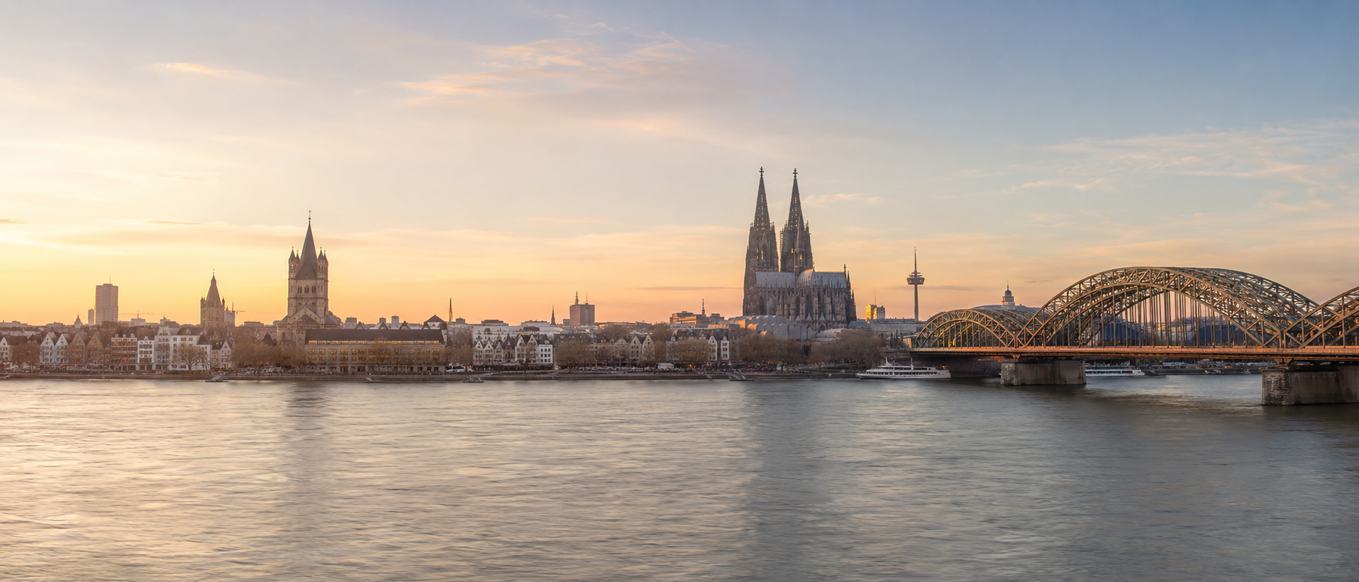 Panoramablick über den Rhein auf den Kölner Dom und die Hohenzollernbrücke im warmen Abendlicht