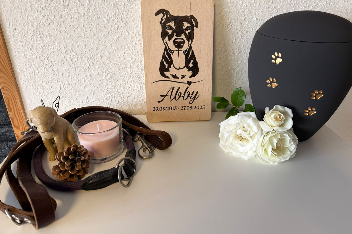 Personalisiertes Gedenkschild für Hund Abby neben Urne, Blumen, Kerze und Halsband